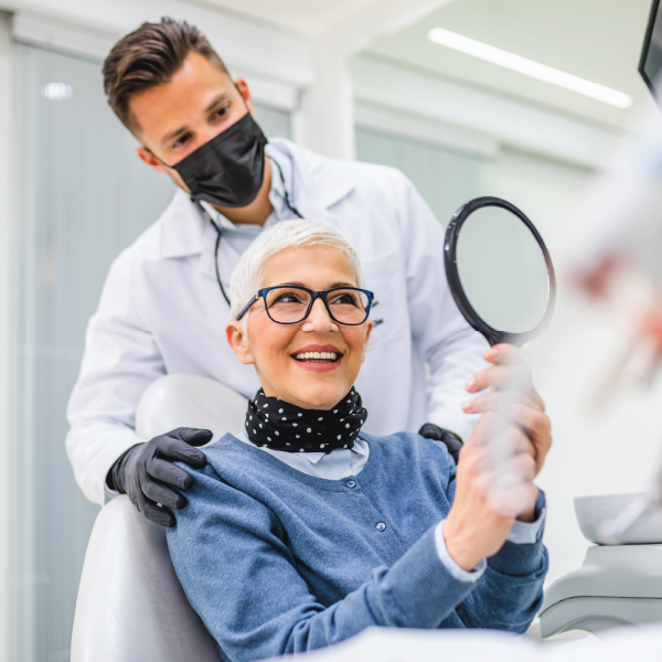  An elderly woman enjoying her new smile woman in a dentist chair smiling and looking in a mirror.