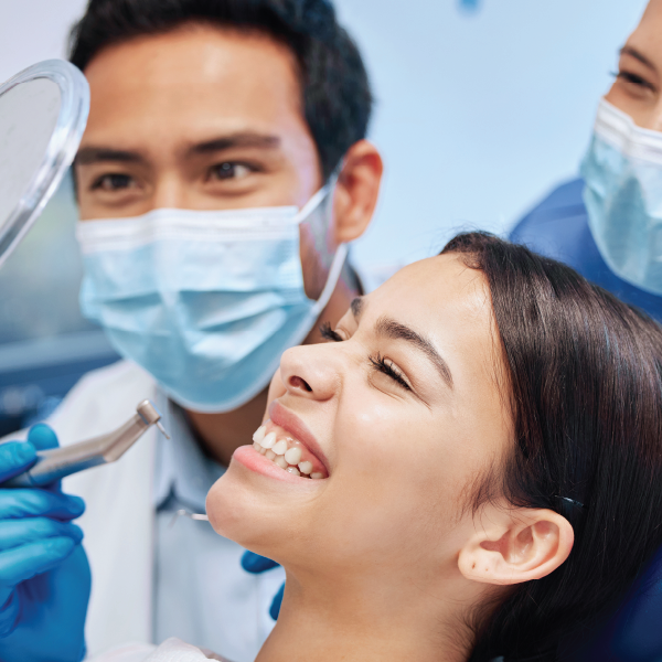  A young woman smiling and looking into a mirror in the dentist chair.