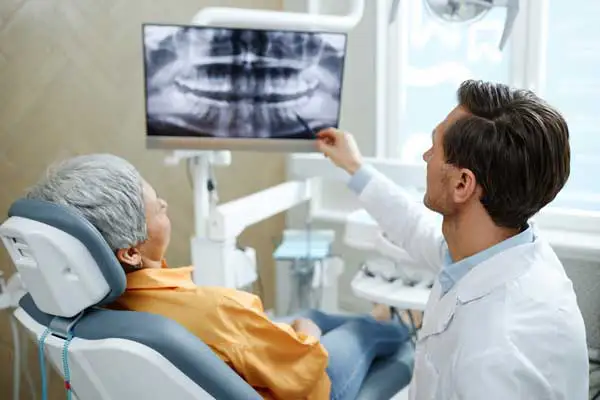 An elderly patient sitting back in the dentist chair as the dentist show points at the x-ray.